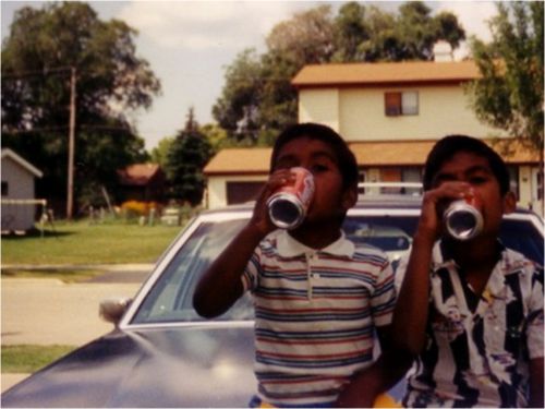 Iqbal drinks Coca-Cola on the hood of a car with his brother in 1990